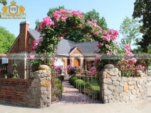 Cánh cổng dùng để dẫn vào ngôi nhà này được bao quanh bởi bức tường đá mộc mạc mà vô cùng độc đáo. Cánh cổng sắt kiểu dáng vòm được trang trí với giàn hoa leo màu hồng khiến cho người nhìn có cảm giác như lạc vào 1 cung điện nhỏ lãng mạn thời xa xưa.